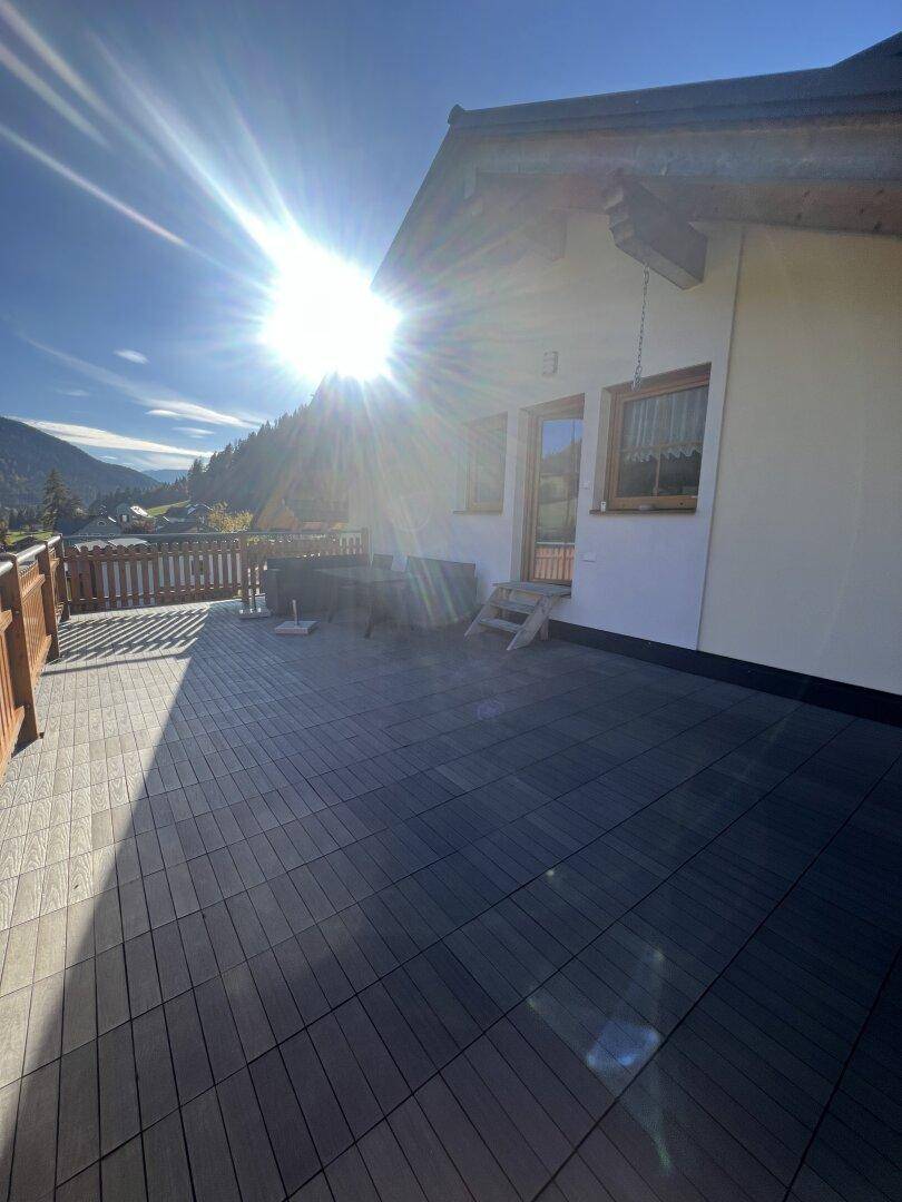 Sonnige, große Terrasse mit dunklem Bodenbelag und Holzgeländer, ideal für entspannte Stunden im Freien.