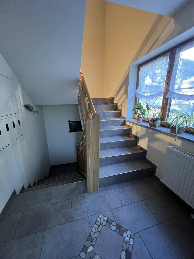 Heller Treppenaufgang mit Fliesenboden, Holzgeländer und einem Fenster für natürliches Licht.