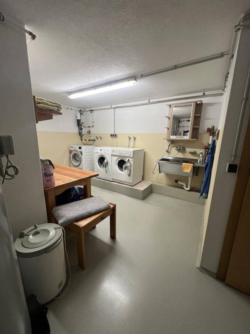 Praktischer Waschraum im Keller mit zwei Waschmaschinen, Spülbecken und einfacher Einrichtung.