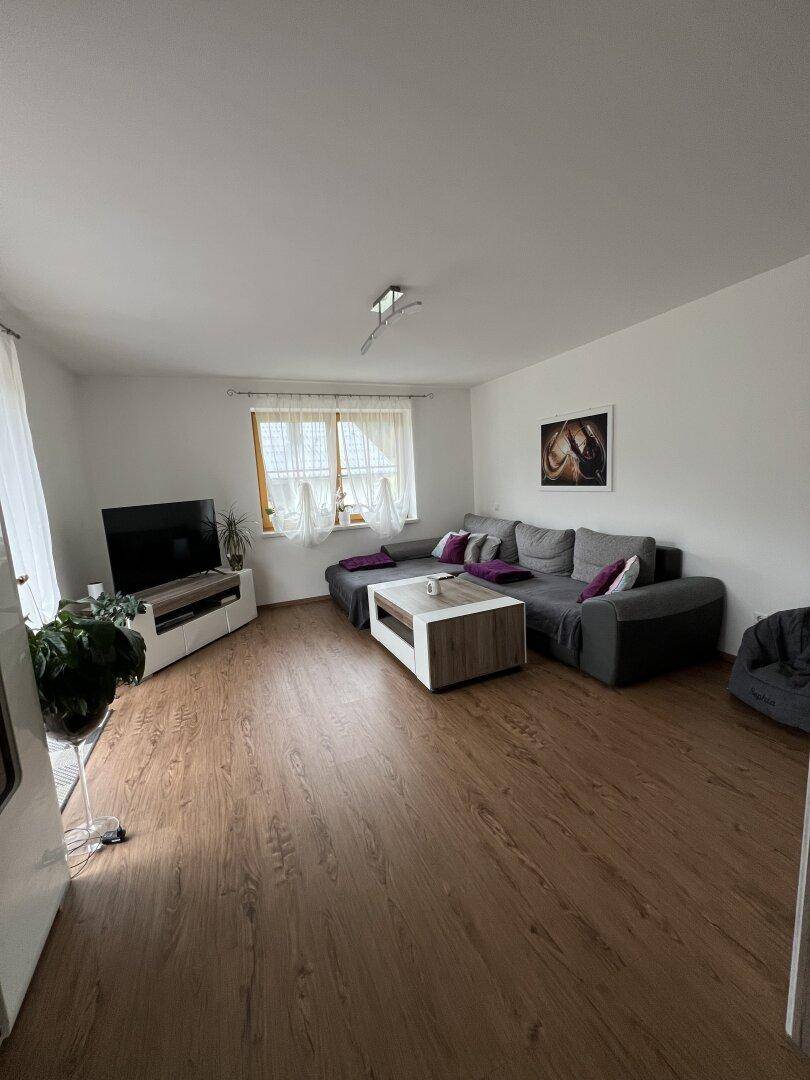Helles Wohnzimmer mit großem grauen Ecksofa, Couchtisch und Fernseher auf Laminatboden.