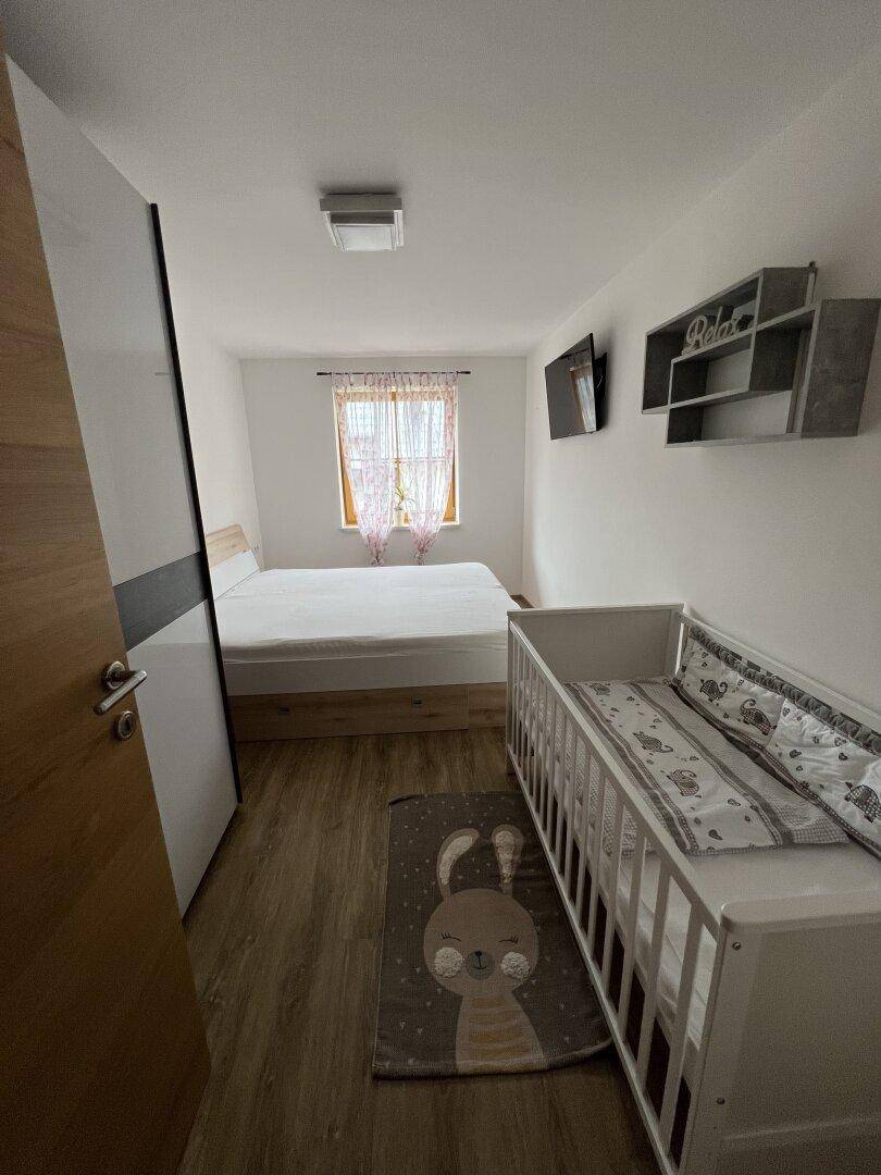 Schlafzimmer mit Doppelbett und Babybett, ausgestattet mit Laminatboden und Fenster.