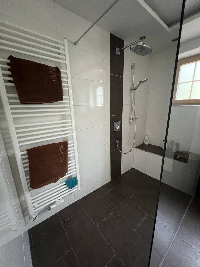 Moderne ebenerdige Dusche mit dunklen und weißen Fliesen, Regendusche und Handtuchheizkörper.