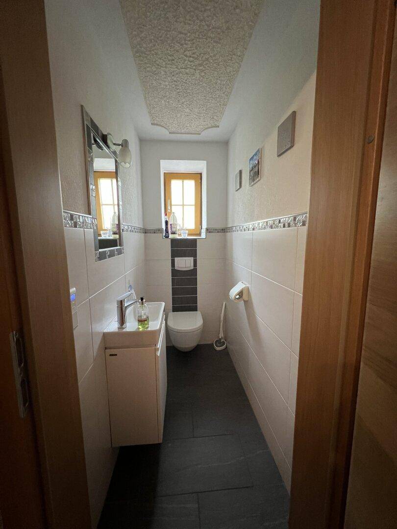 Schmale Gästetoilette mit dunklem Fliesenboden, wandhängendem WC und kleinem Fenster für Tageslicht.