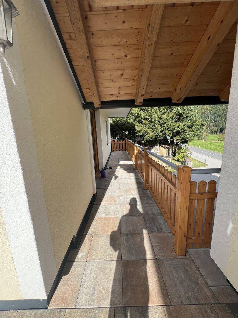 Überdachter Außenbereich oder Loggia mit Fliesenboden und rustikalem Holzgeländer.