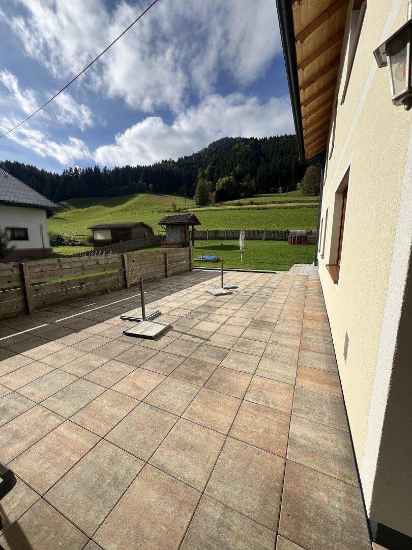 Weitläufige gepflasterte Terrasse mit Blick auf den Garten und die umliegende grüne Landschaft.