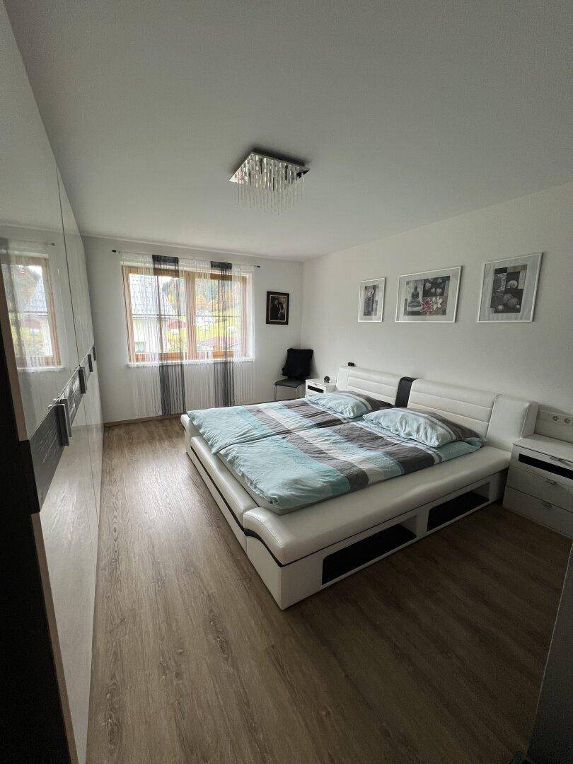 Schlafzimmer mit großem weißen Doppelbett, dunklen Kleiderschränken und Laminatboden.