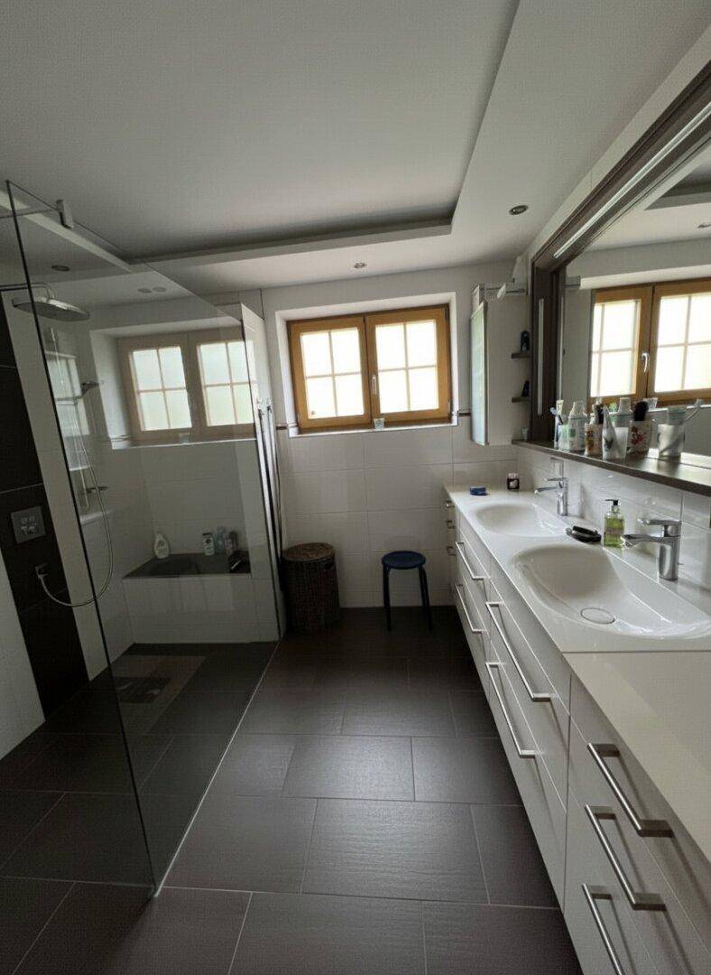 Modernes Badezimmer mit Doppelwaschbecken, großem Spiegel, ebenerdiger Dusche und Fenster.