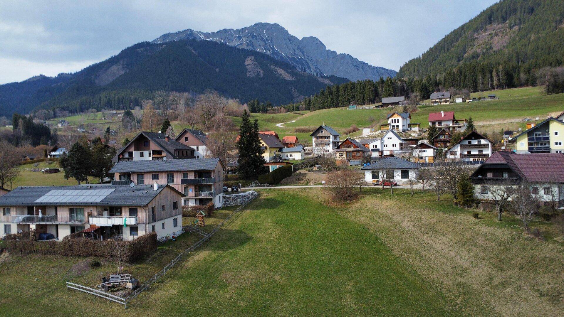 Panoramablick auf ein idyllisches Dorf mit traditionellen Häusern vor einer beeindruckenden Bergkulisse.