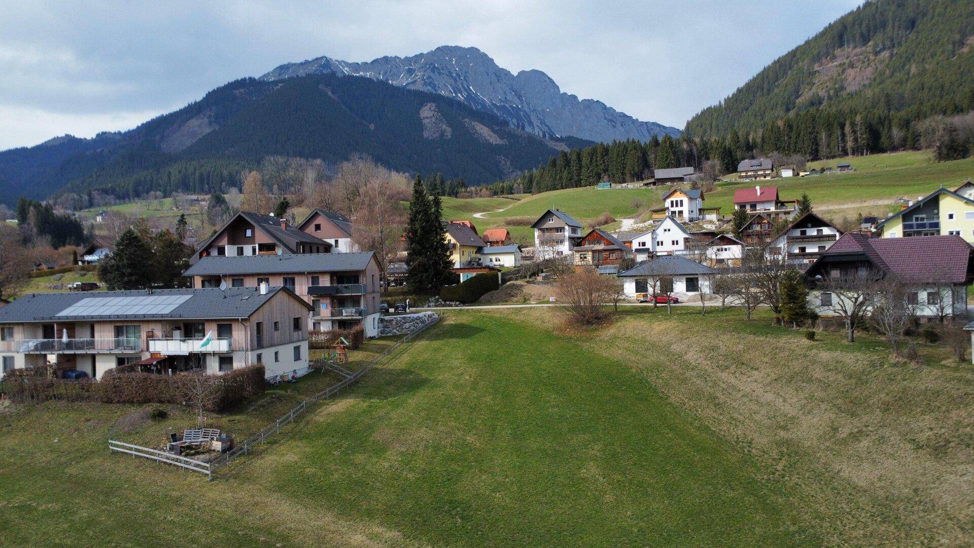 Panoramablick auf ein idyllisches Dorf mit traditionellen Häusern vor einer beeindruckenden Bergkulisse.