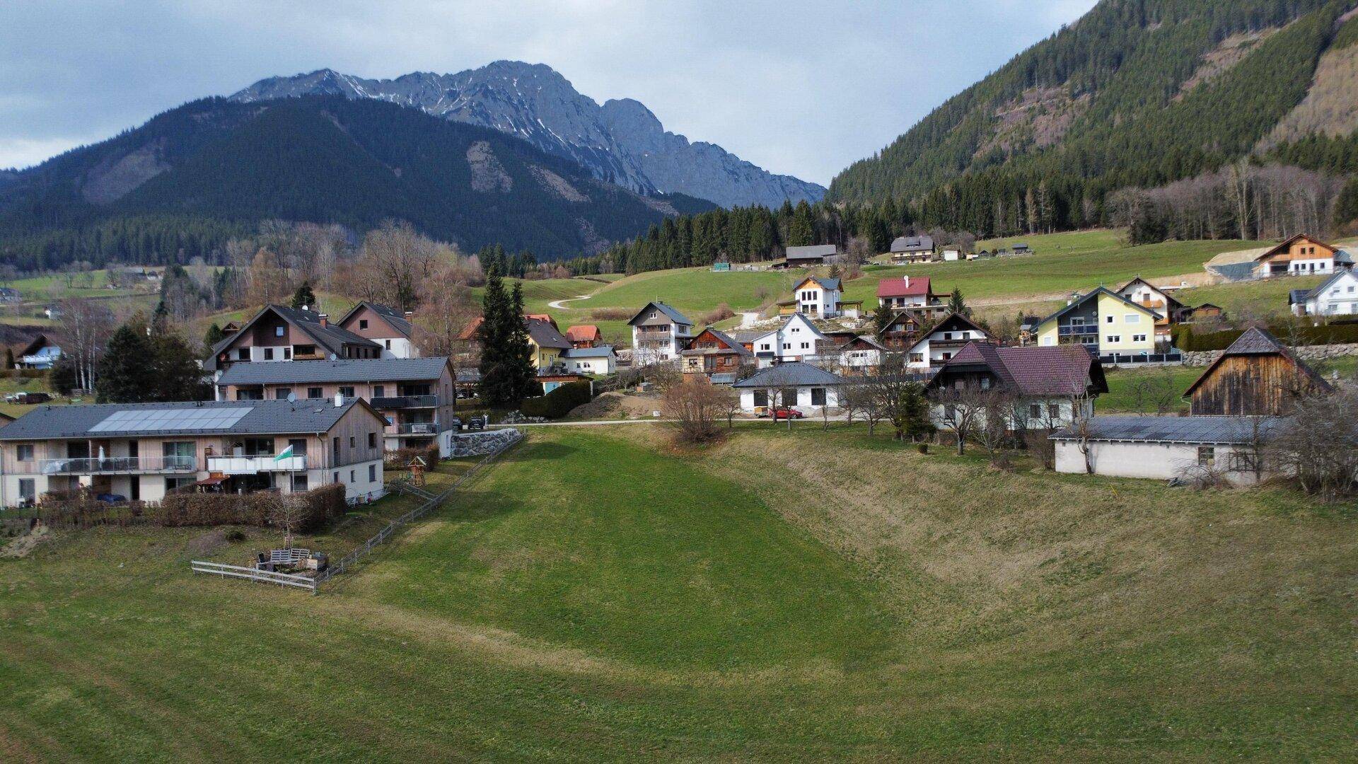 Panoramablick auf ein idyllisches Dorf mit traditionellen Häusern vor einer beeindruckenden Bergkulisse.