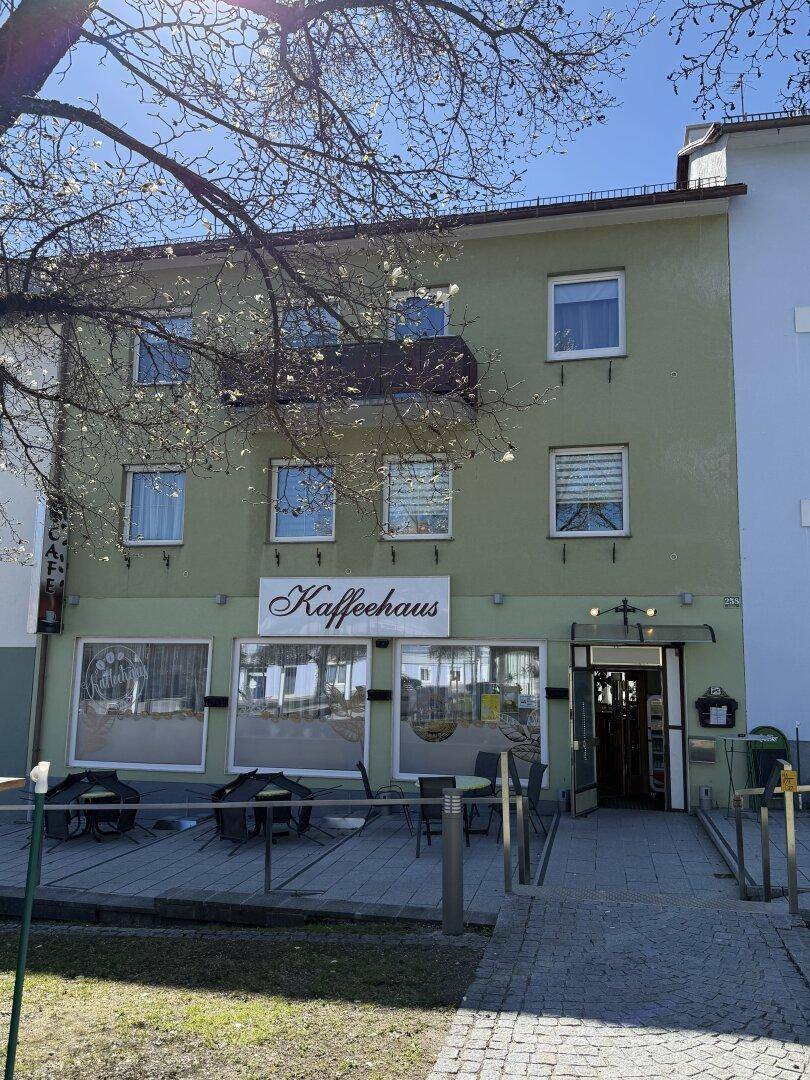 Fassade eines grünen Gebäudes mit Café im Erdgeschoss und einem kleinen Balkon.