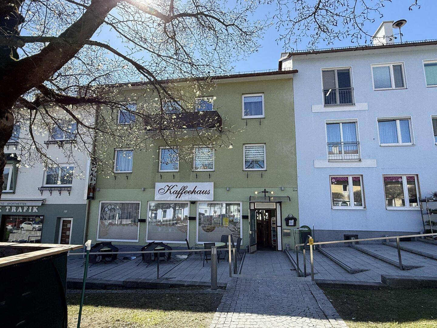 Grünes Gebäude mit Café und angrenzendem blauen Wohnhaus an einem sonnigen Tag.