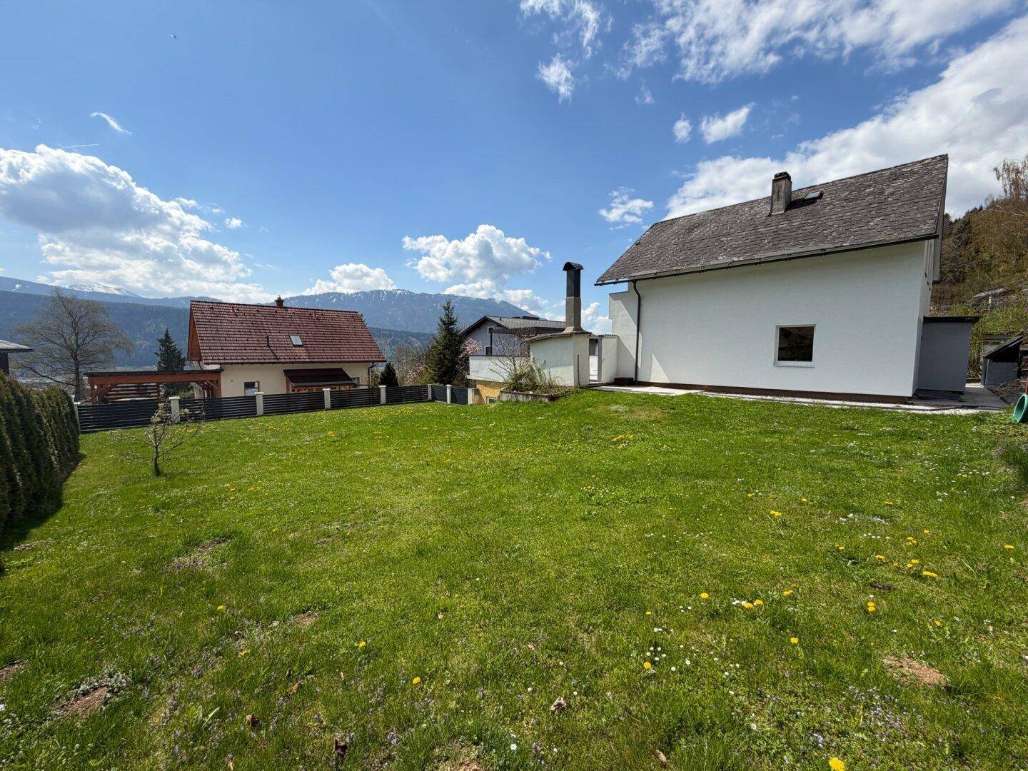 Großer grüner Garten mit Rasenfläche und Blick auf die umliegenden Berge und Häuser.