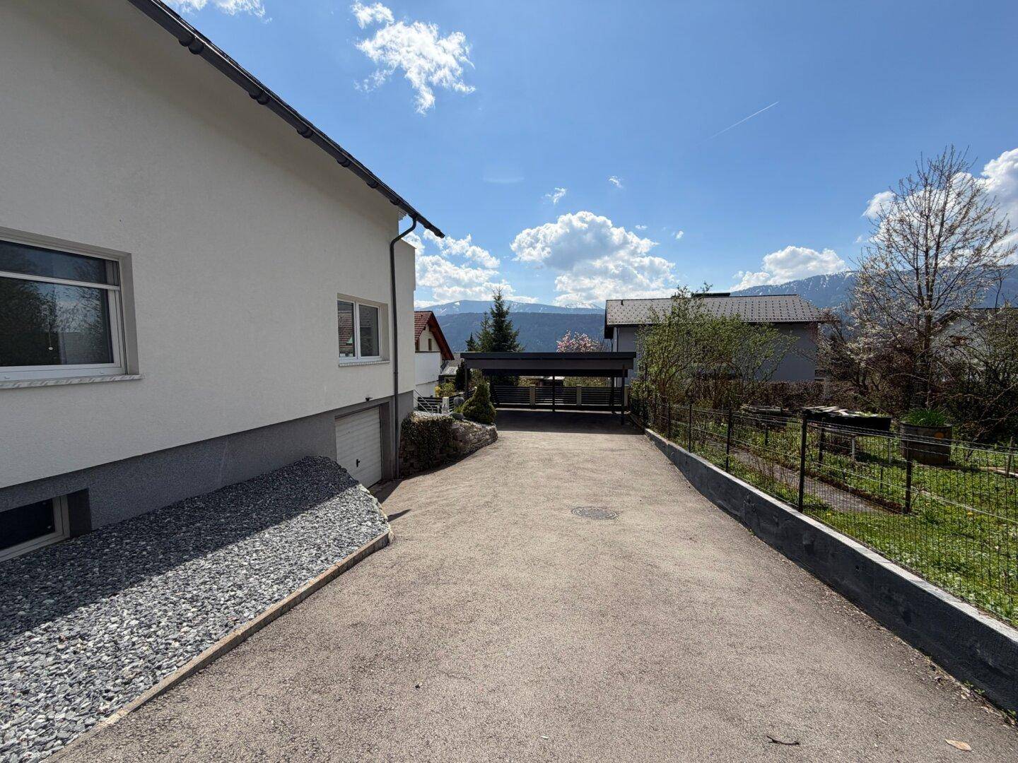 Auffahrt zum Haus mit Carport und Blick auf die umliegende Landschaft unter blauem Himmel.