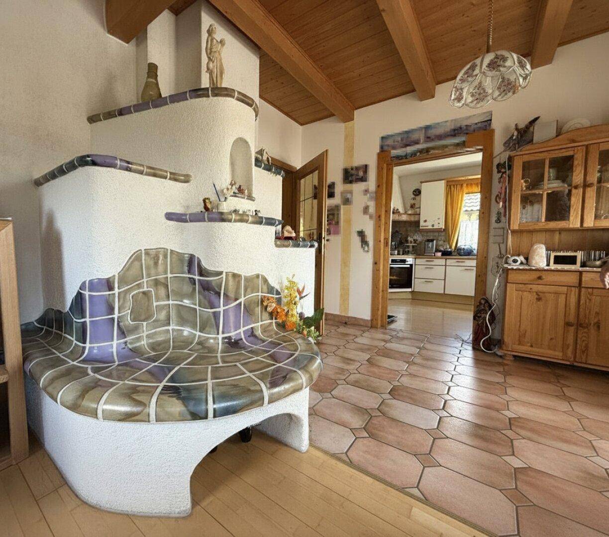 Traditionelles Wohnzimmer mit einem großen Kachelofen, Holzbalkendecke und Fliesenboden.