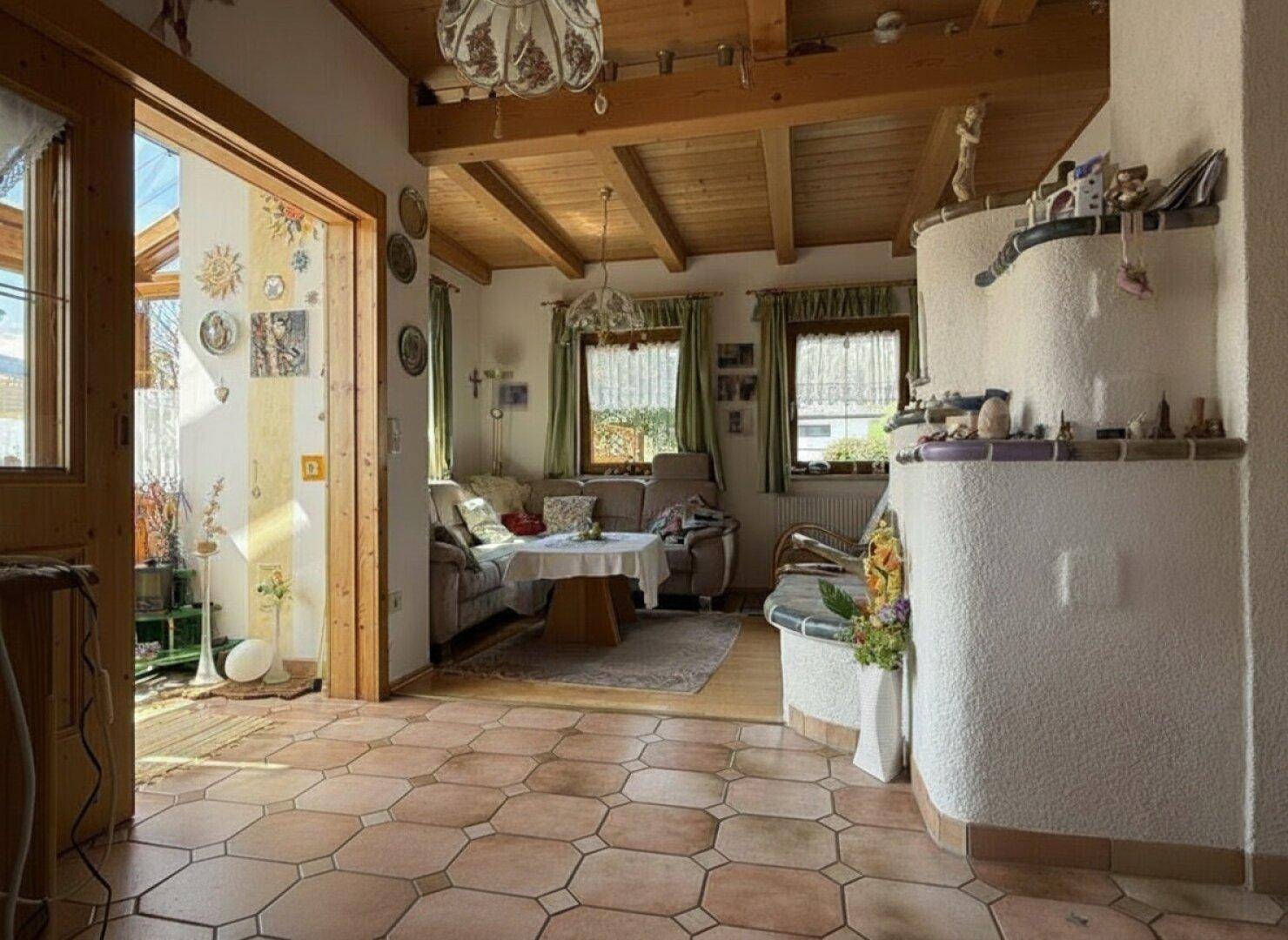 Geräumiges Wohnzimmer mit Kachelofen, Holzbalkendecke und Zugang zum Wintergarten.