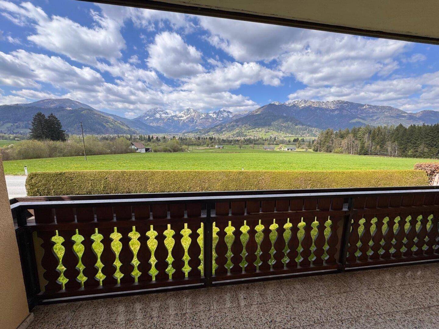 Panoramablick vom Balkon auf die weite grüne Landschaft und die majestätischen Berge.