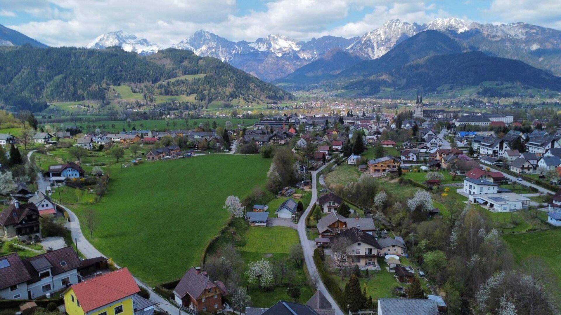 Luftaufnahme einer ländlichen Siedlung eingebettet in grüne Felder und umgeben von majestätischen Bergen.