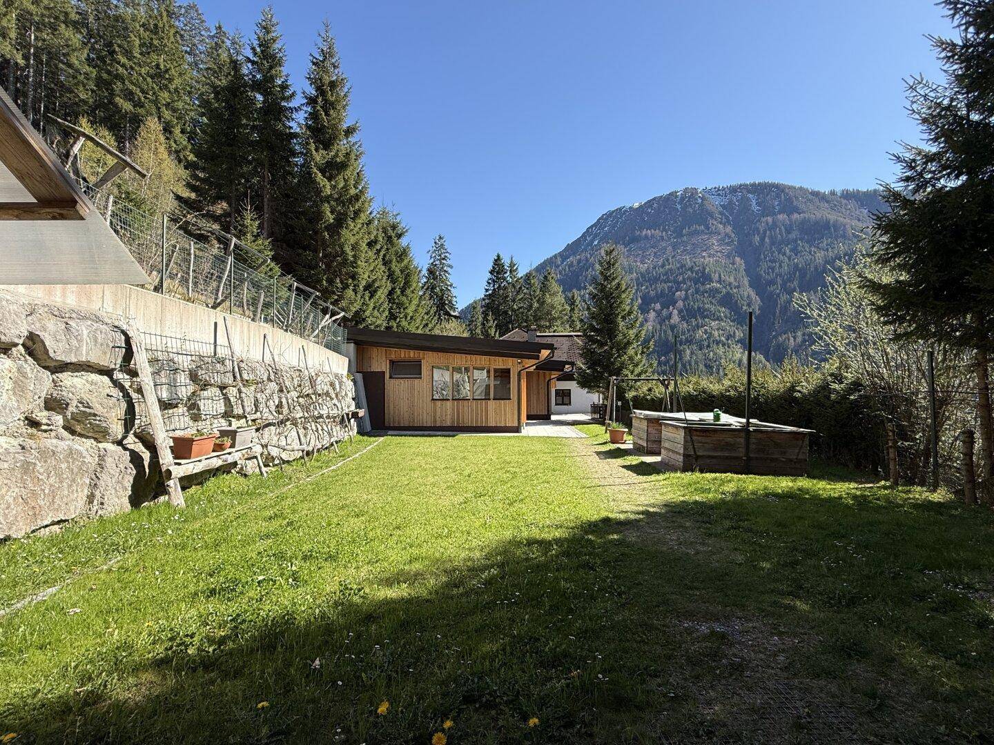 Grüner Gartenbereich mit kleinem Holzhaus und Blick auf die majestätischen Berge.