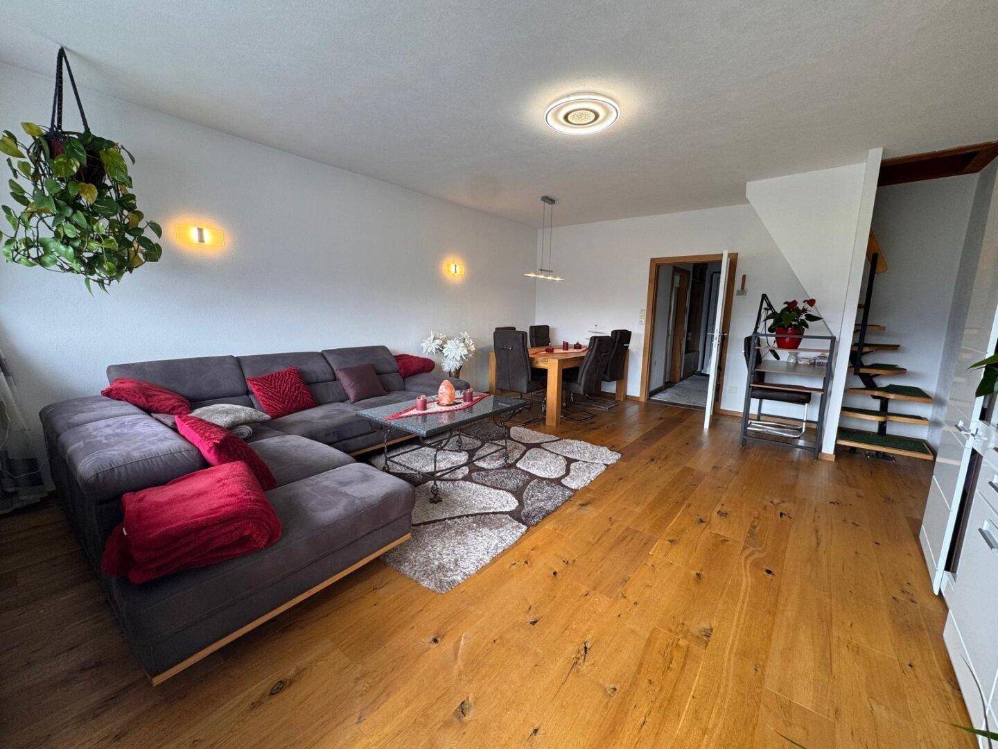 Heller Wohnbereich mit bequemer Couch, Holzboden und offenem Übergang zum Essbereich und Treppe.
