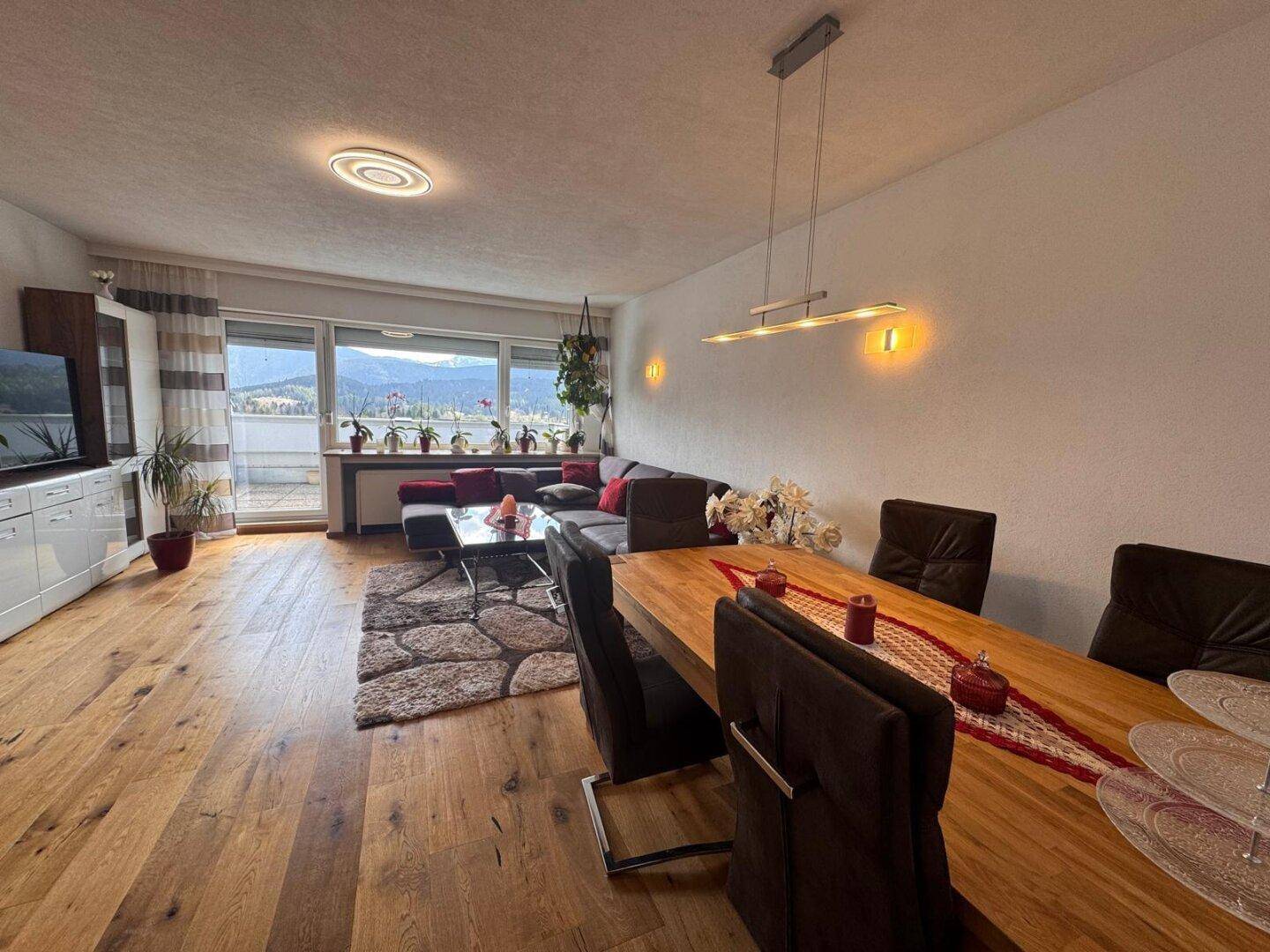 Geräumiger offener Wohn-Essbereich mit Holzboden, großem Esstisch und Bergblick vom Balkon.
