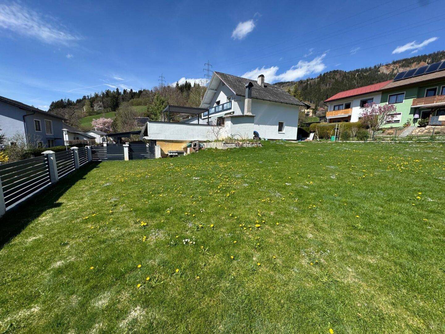 Haus mit Satteldach und großem Garten auf einem sonnigen Grundstück mit Bergblick.