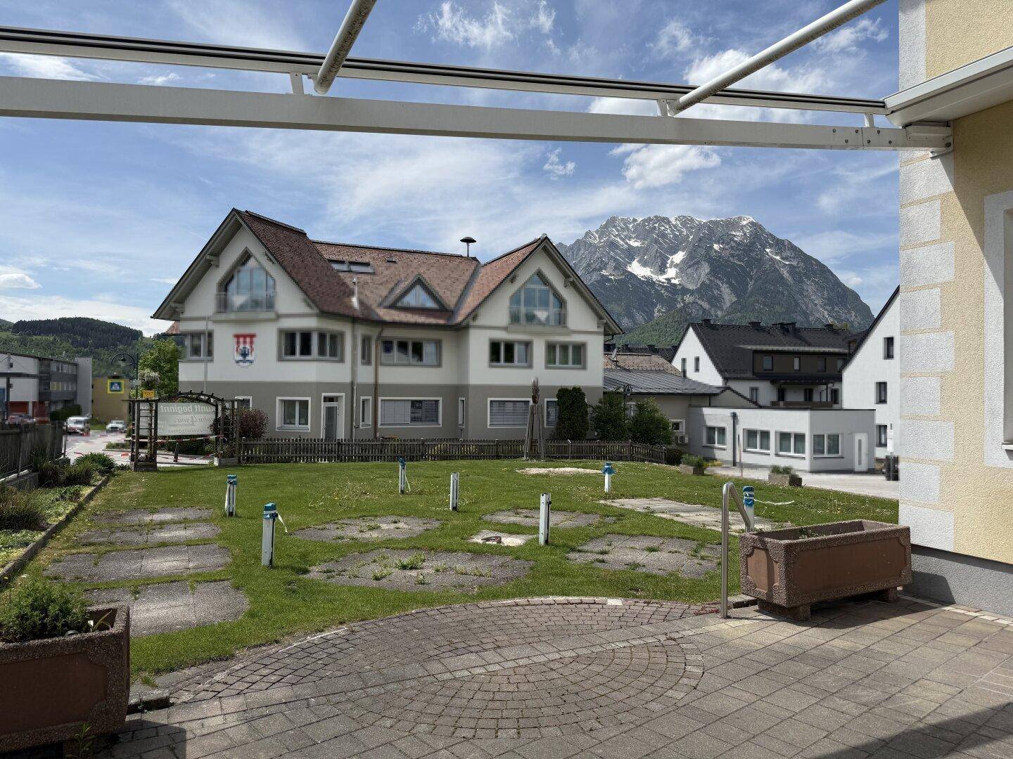 Blick auf ein Gebäude mit Satteldach und Bergpanorama, umgeben von Grünflächen und Parkplätzen.