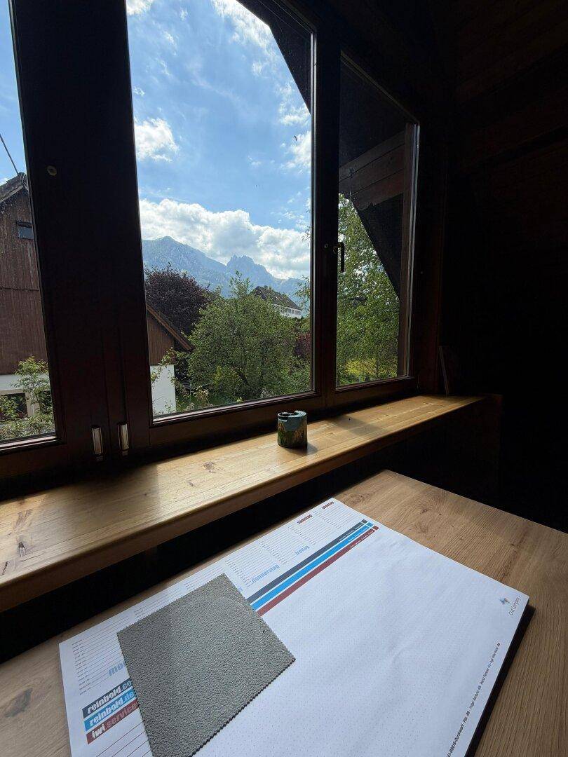Fenster mit Bergblick von einem Innenraum aus, mit Holztisch und natürlichem Licht.