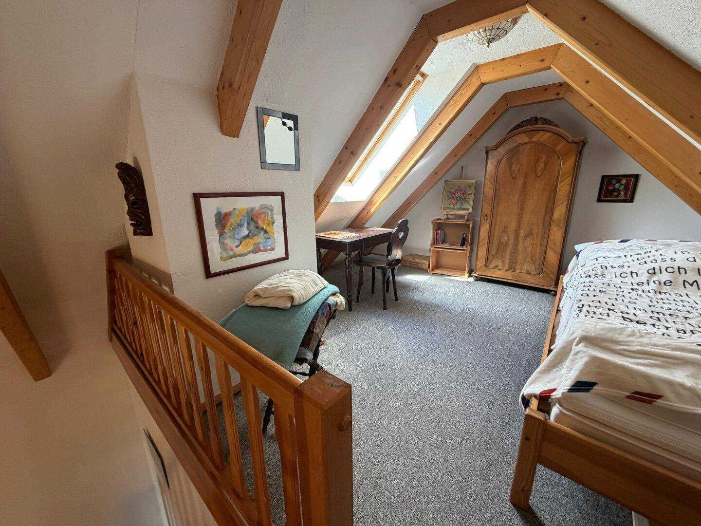 Gemütliches Schlafzimmer im Dachgeschoss mit Dachschrägen, Holzbalken und Teppichboden.