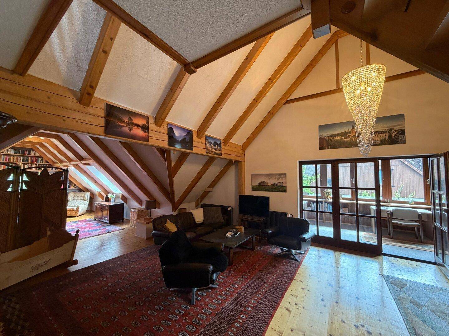 Geräumiges Wohnzimmer im Dachgeschoss mit sichtbaren Holzbalken und hohen Decken.