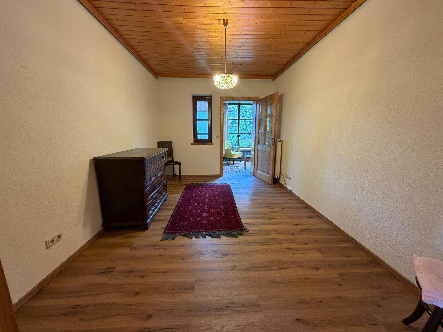 Helles Zimmer mit Holzboden und Zugang zu einem Wintergarten, ideal als Schlafzimmer.