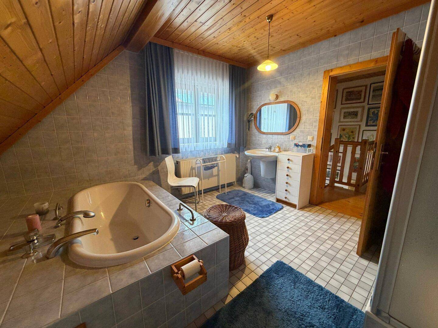 Helles Badezimmer im Dachgeschoss mit Badewanne, Fenster und Holzdecke.