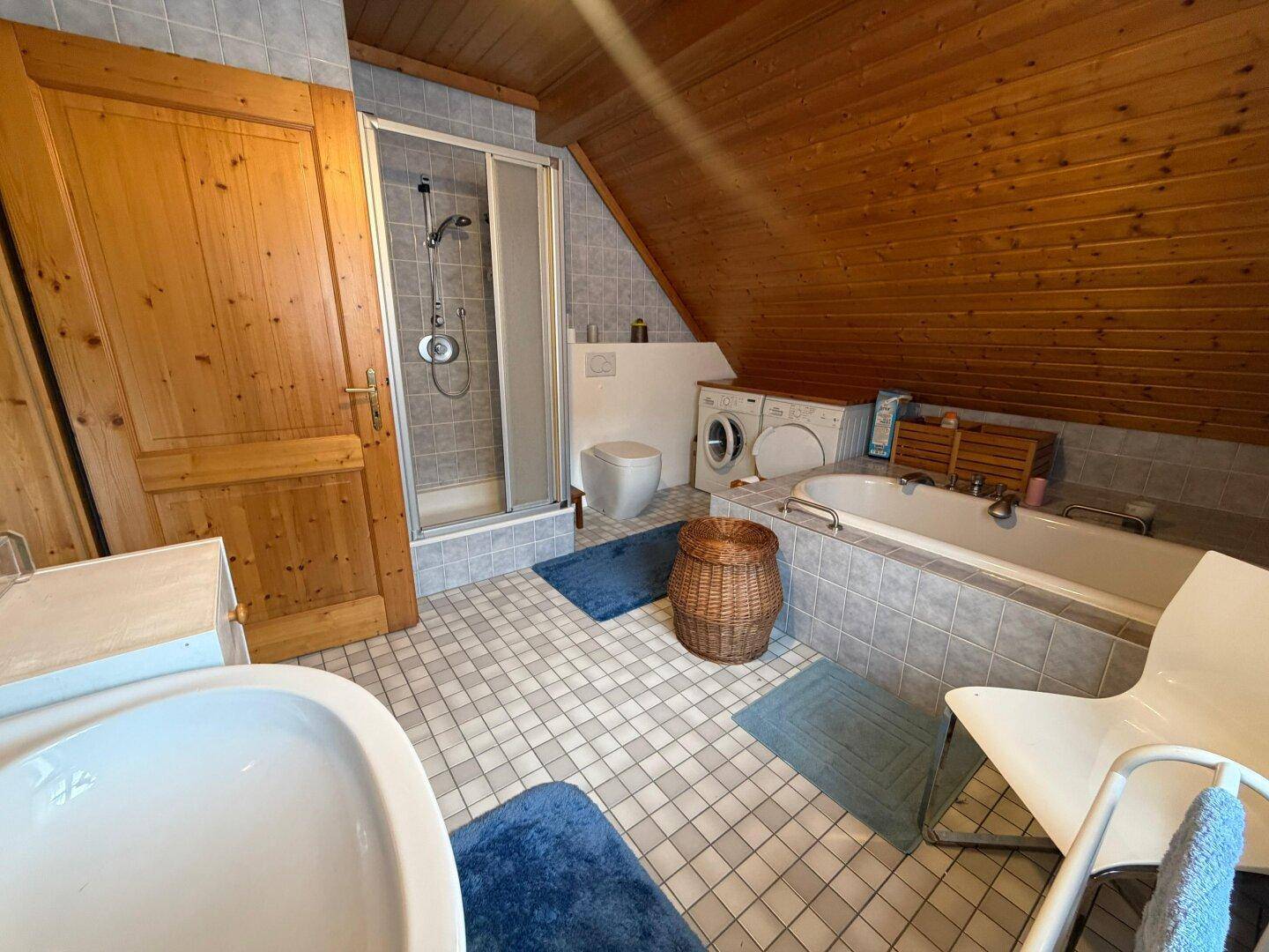 Badezimmer im Dachgeschoss mit Badewanne, Dusche und Waschmaschine.