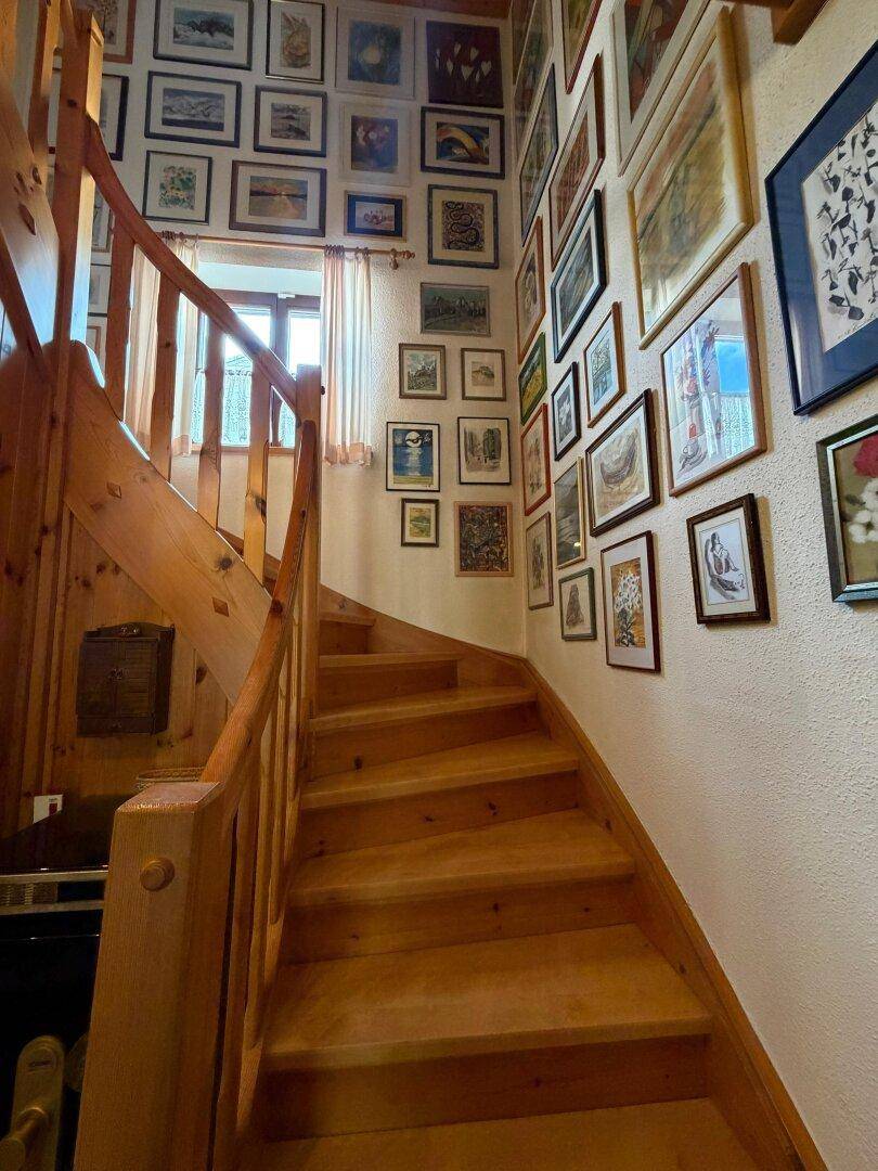Holztreppe mit vielen gerahmten Bildern an der Wand, die zum Obergeschoss führt.