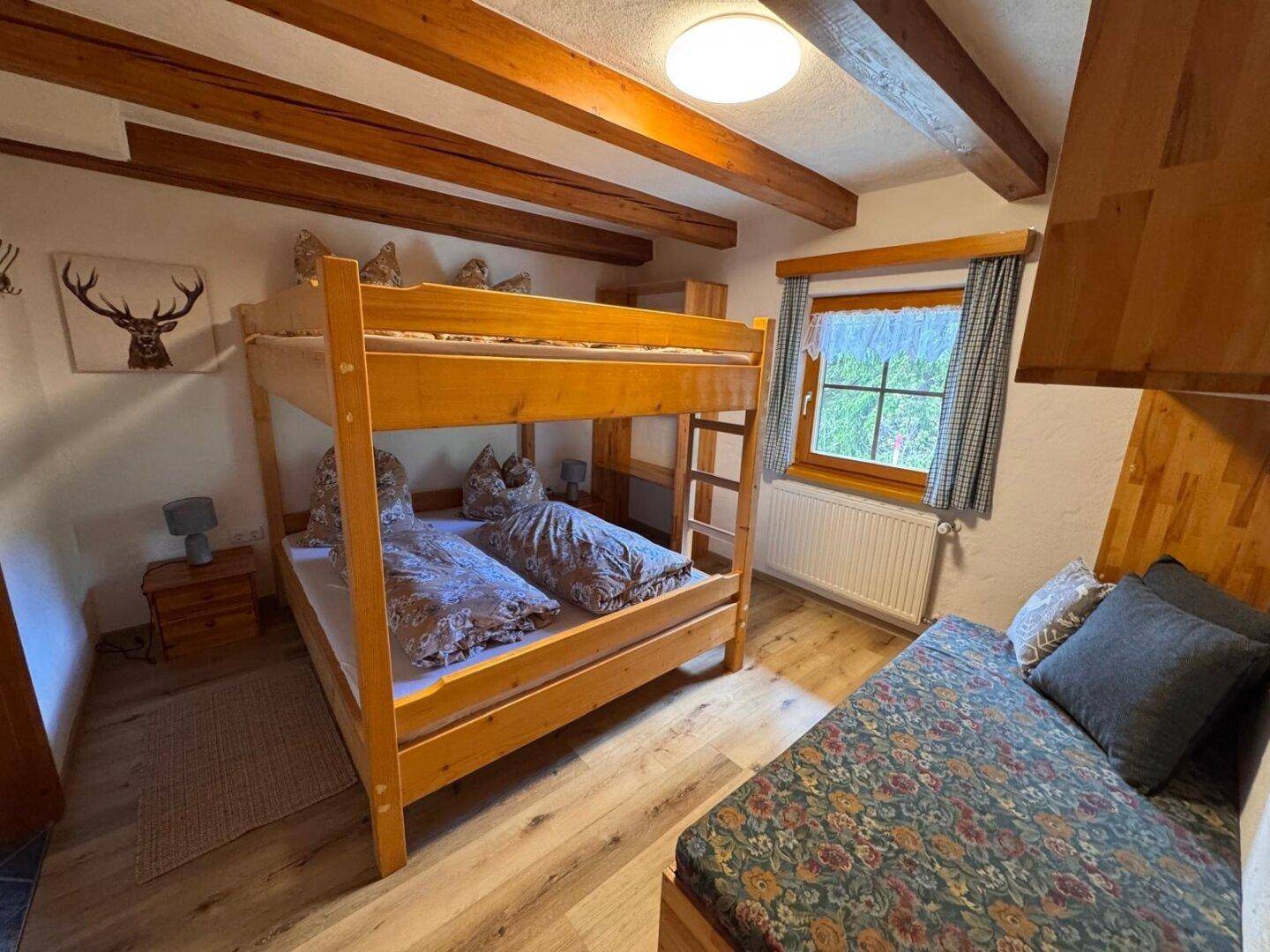 Rustikales Schlafzimmer mit Etagenbett, Holzbalken und Hirschgeweih-Dekoration.
