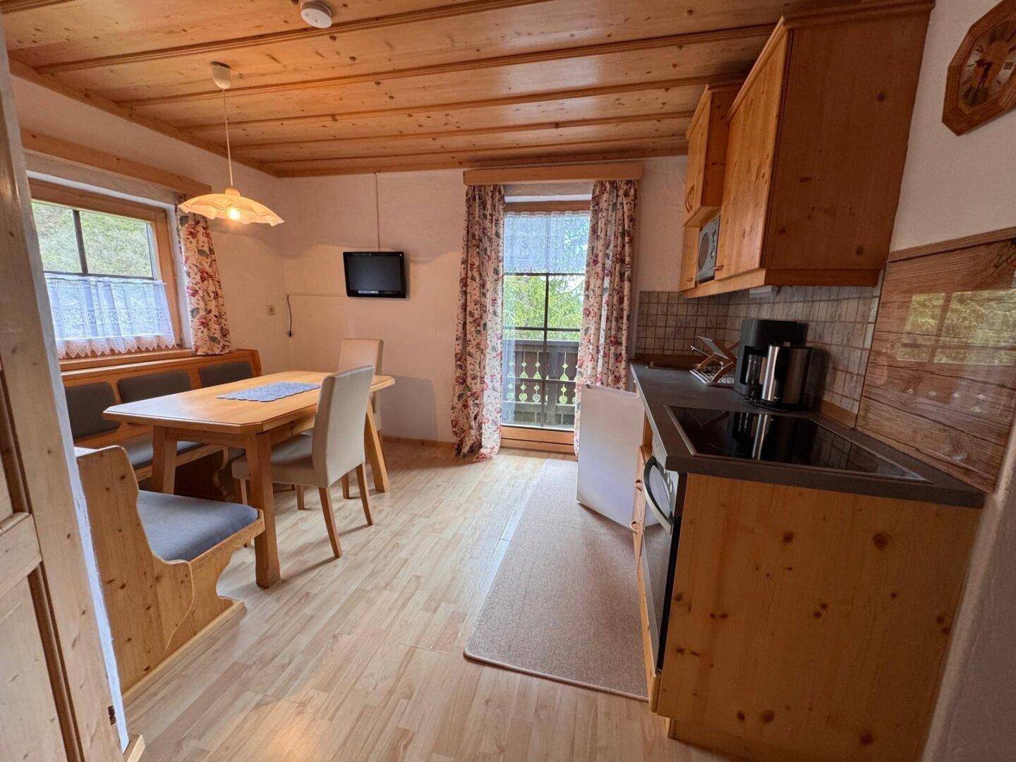 Gemütliche Wohnküche im Landhausstil mit Holzbalkendecke und Essbereich.
