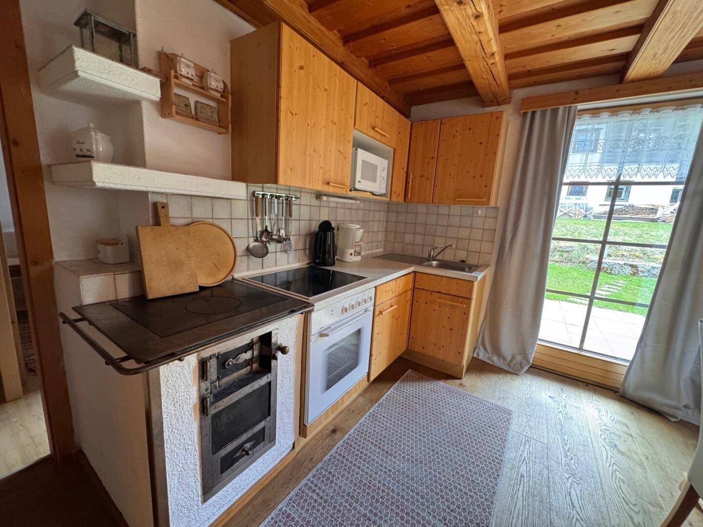 Traditionelle Küche mit Holzschränken, Kachelofen und Zugang zum Garten.