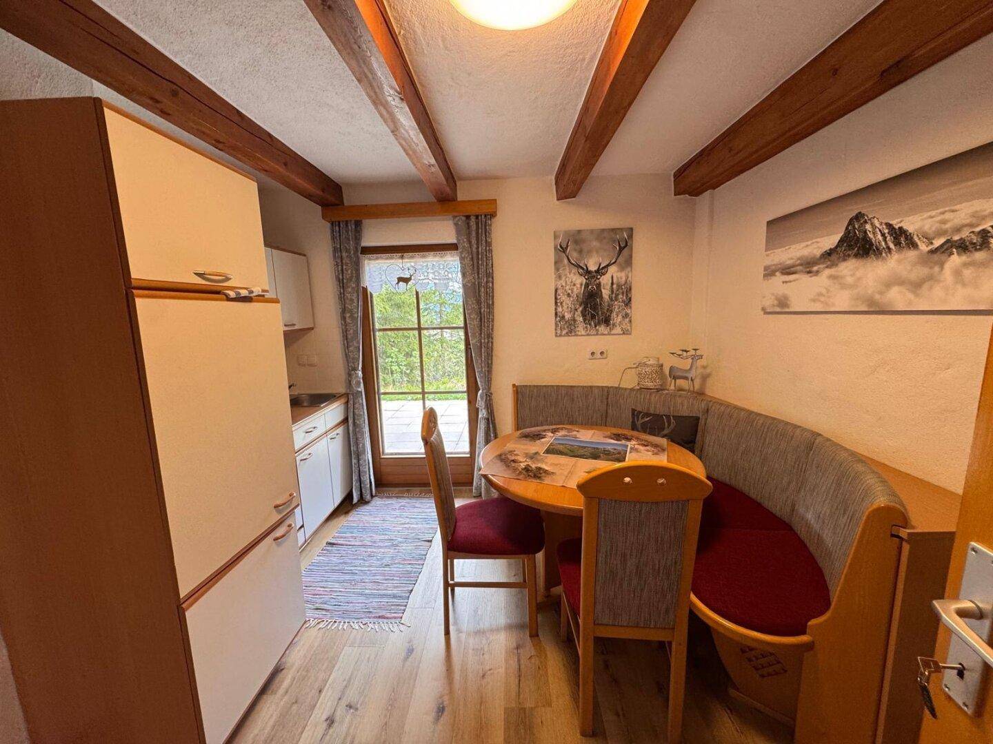 Kleine Küche mit Essecke und Kühlschrank, Holzbalken und Fenster mit Bergblick.