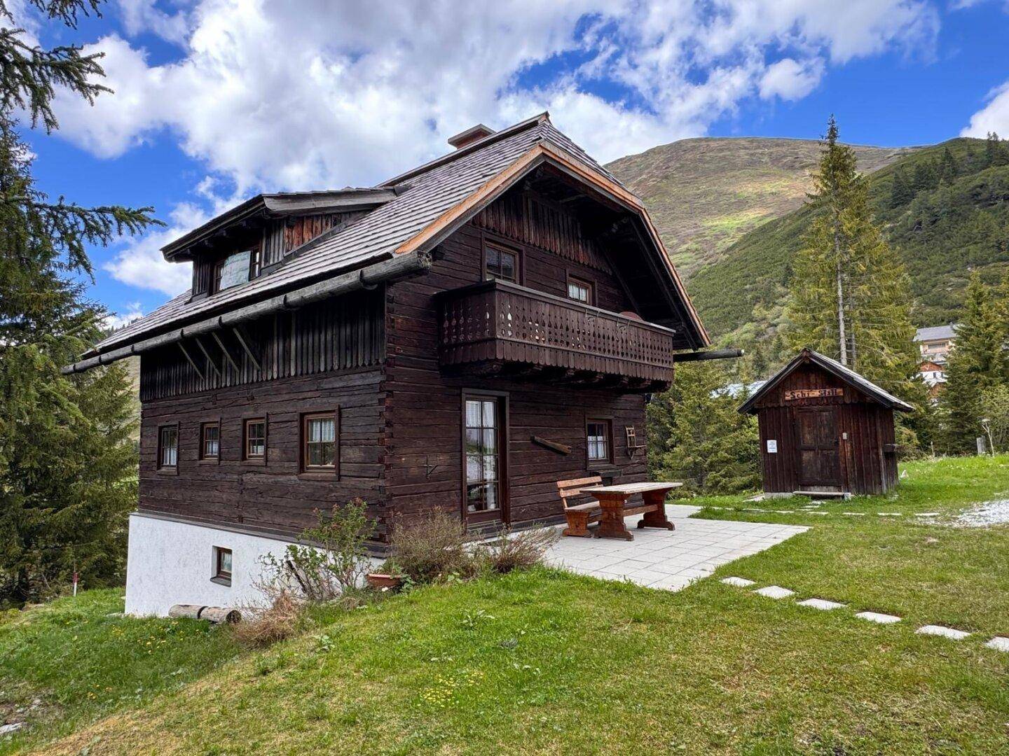 Charmantes Holzchalet mit Balkon und Terrasse, eingebettet in die Bergwelt unter blauem Himmel.