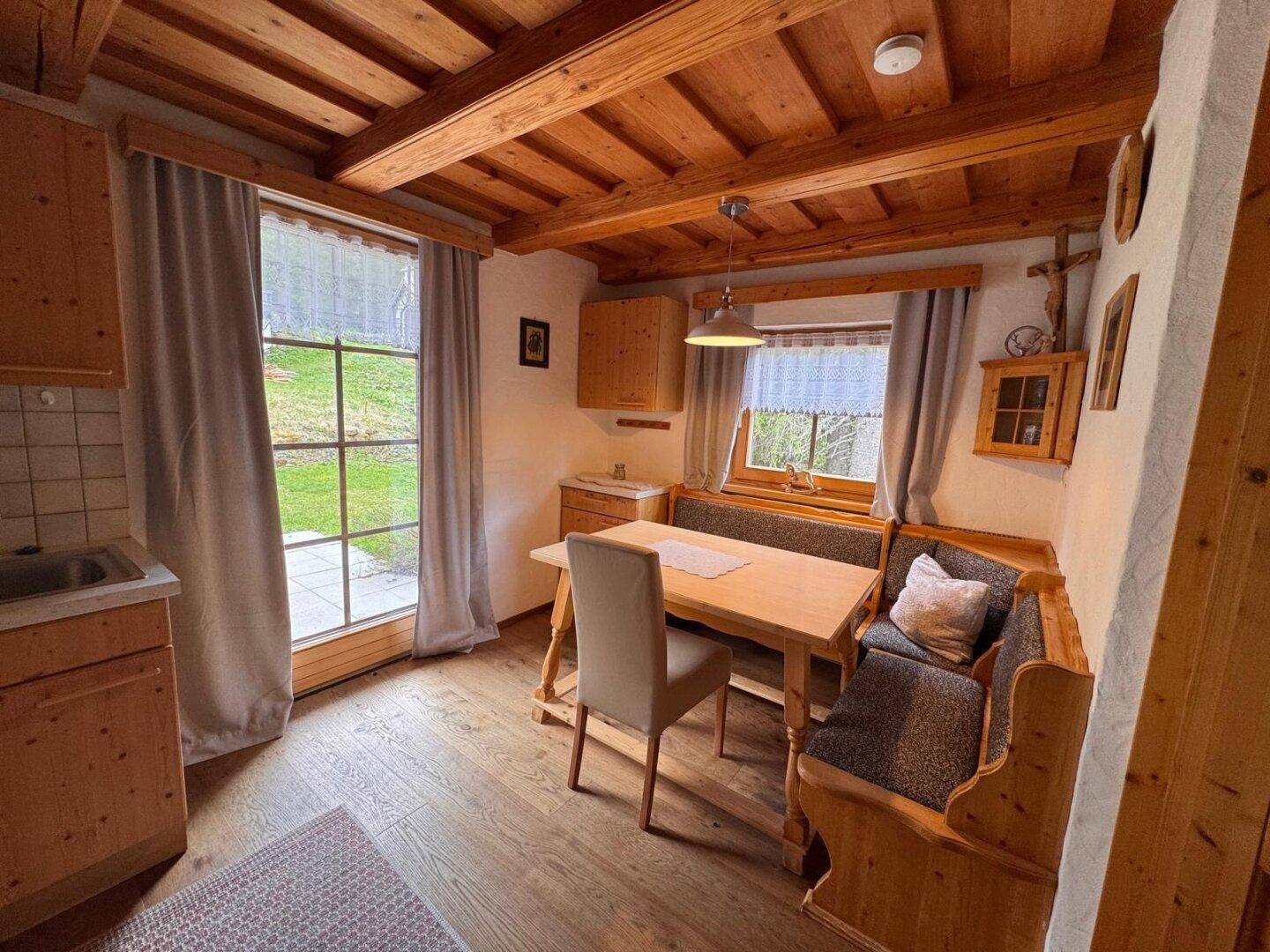 Gemütliche Wohnküche mit Holzbalkendecke, Essecke und Zugang zum Außenbereich.