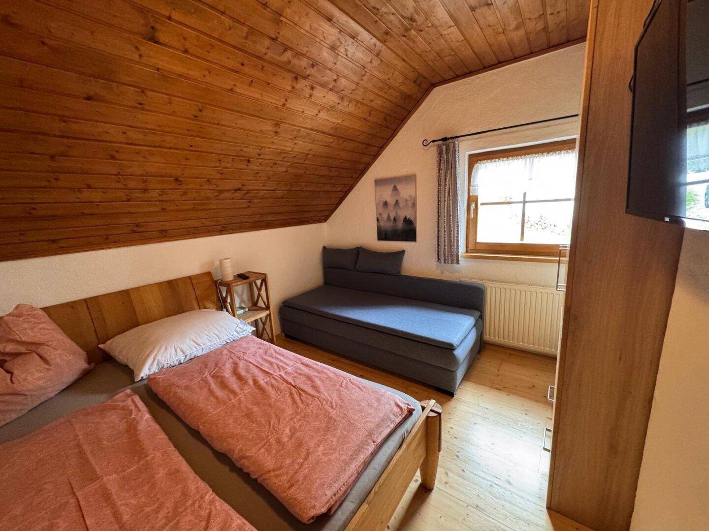 Schlafzimmer im Dachgeschoss mit Holztäfelung, Doppelbett und Schlafsofa.
