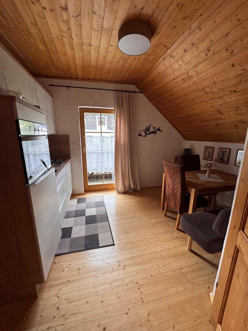 Dachgeschossküche mit Essbereich, Holzboden und Zugang zum Außenbereich.