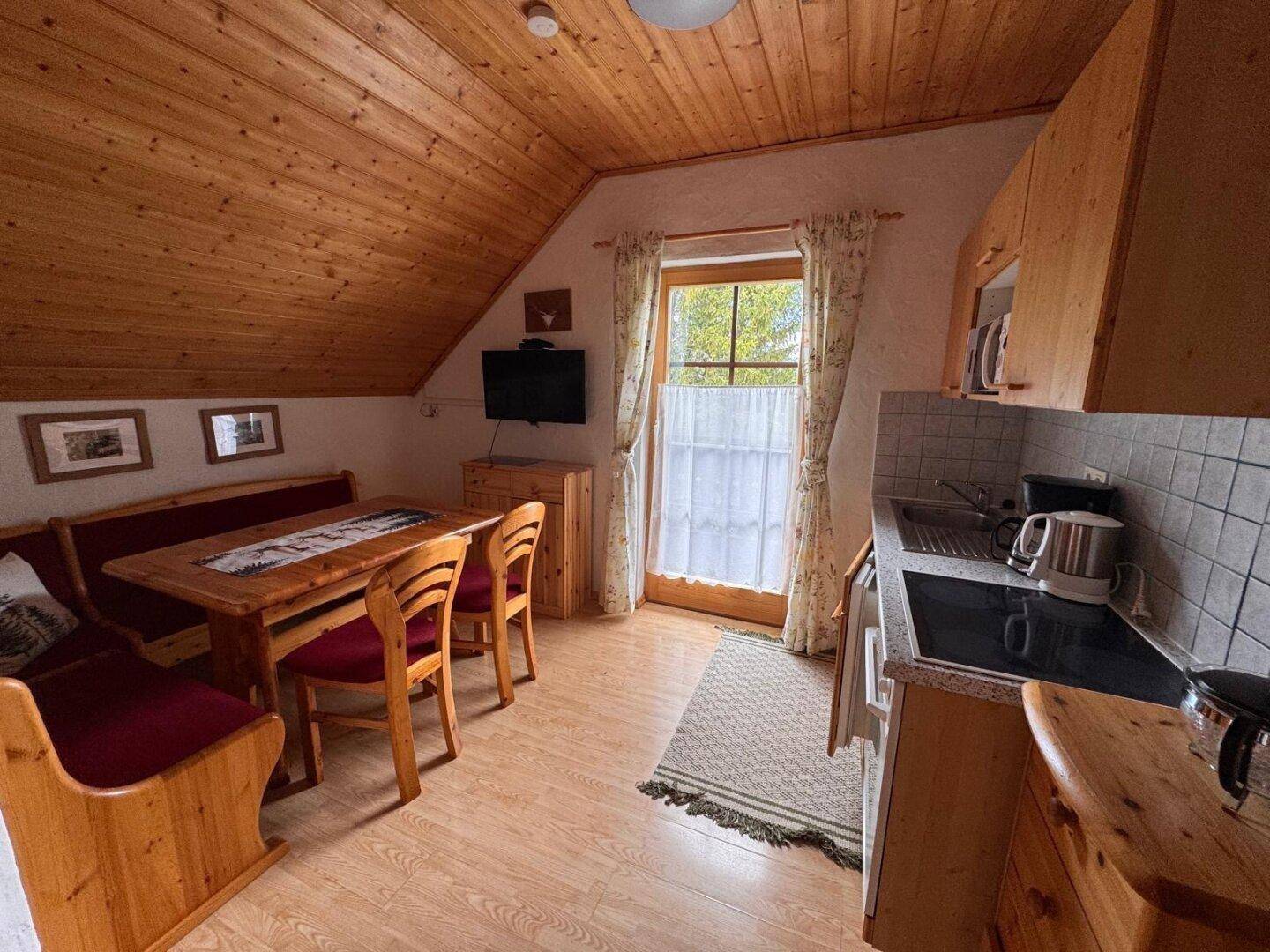 Dachgeschossküche mit Essecke, Holztäfelung und Zugang zum Balkon.