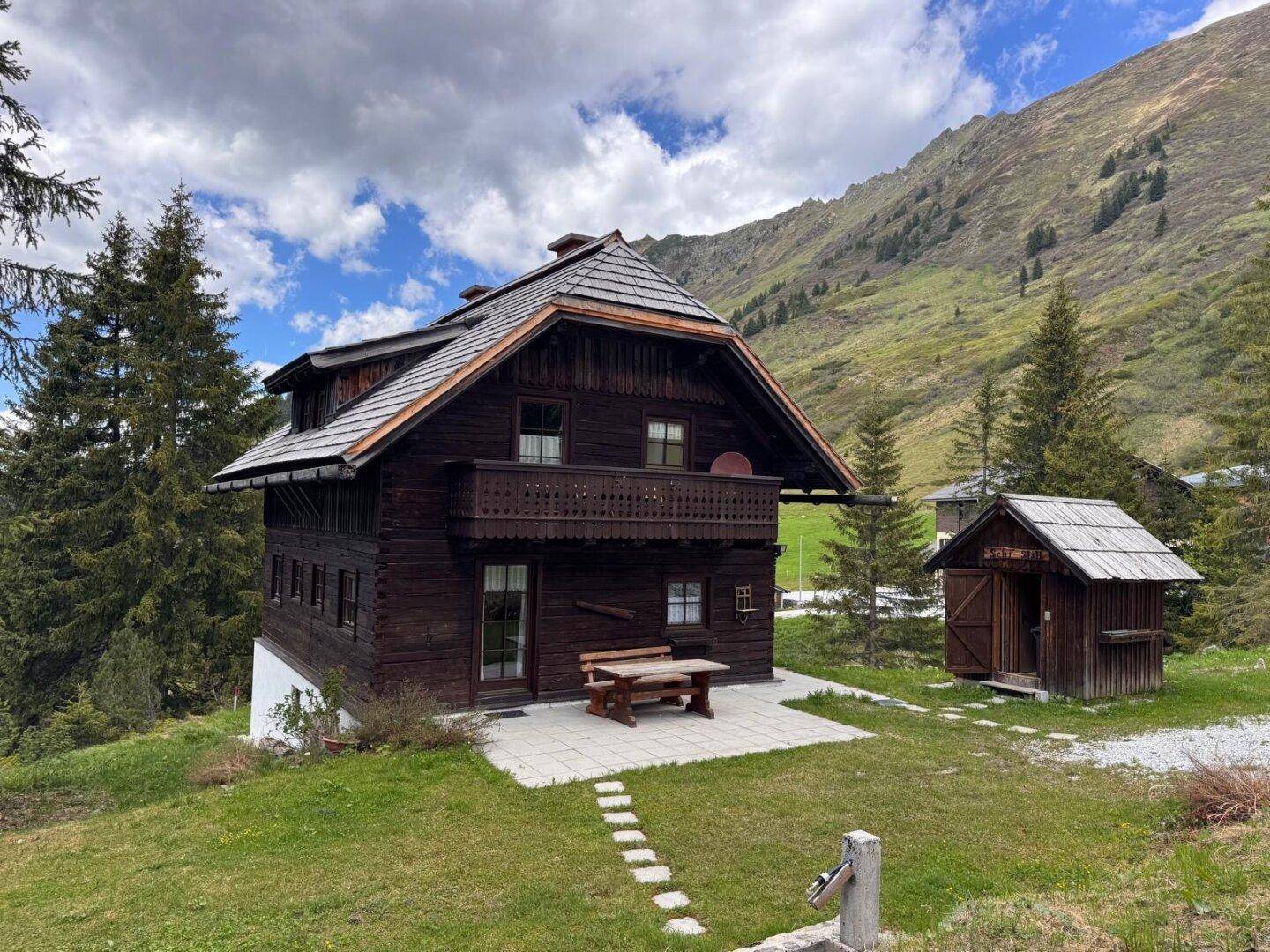 Traditionelles Holzhaus in alpiner Landschaft mit Bergblick und kleiner Terrasse.