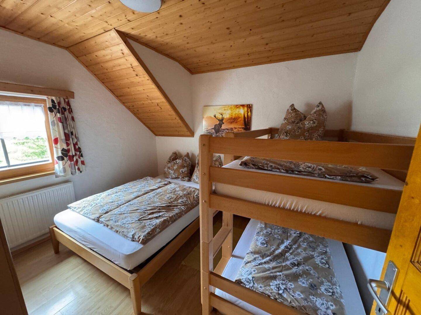 Schlafzimmer im Dachgeschoss mit Doppelbett und Etagenbett, Holztäfelung und Fenster.