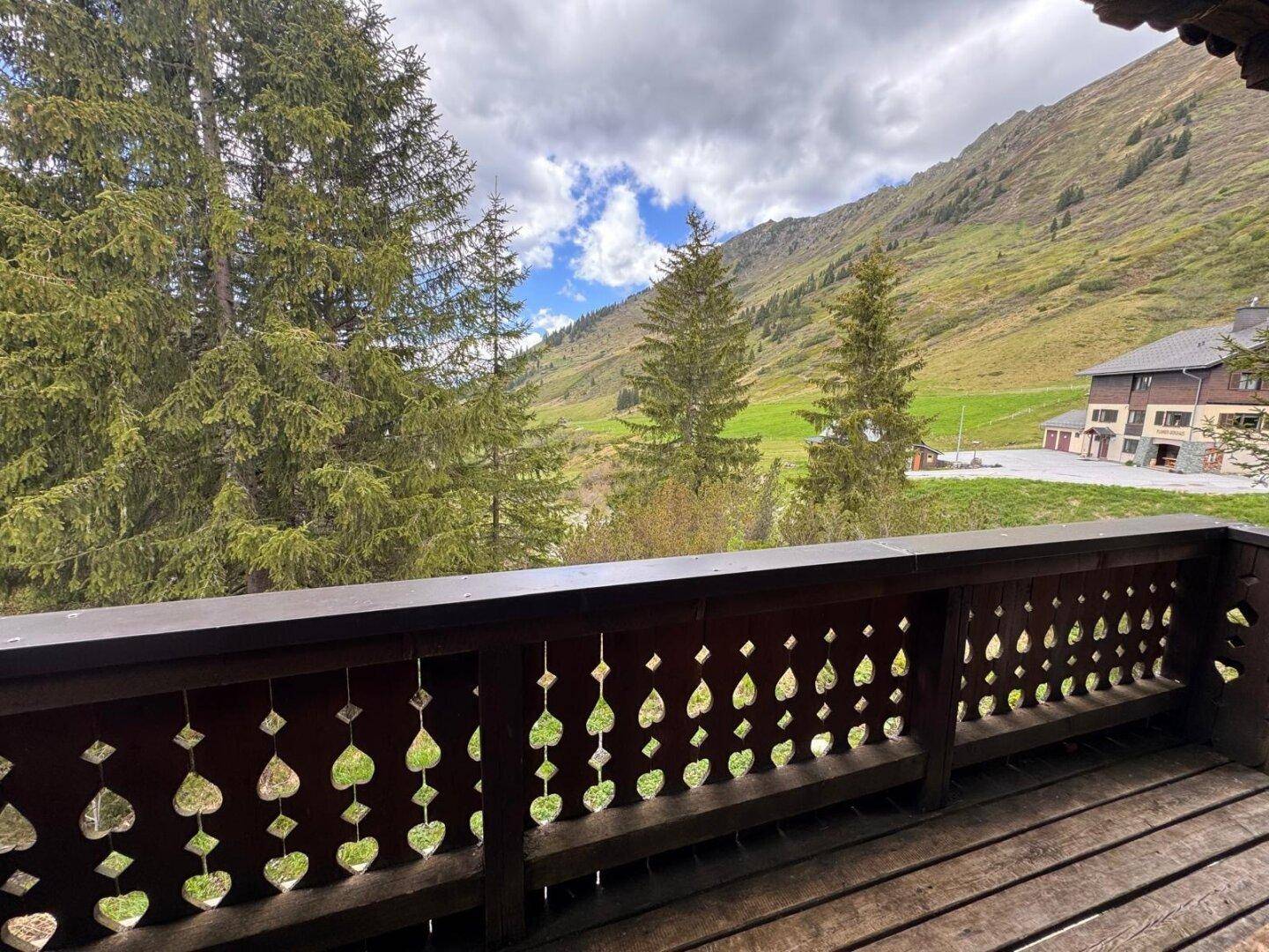 Holzbalkon mit geschnitztem Geländer und weitem Blick auf die umliegende Berglandschaft.
