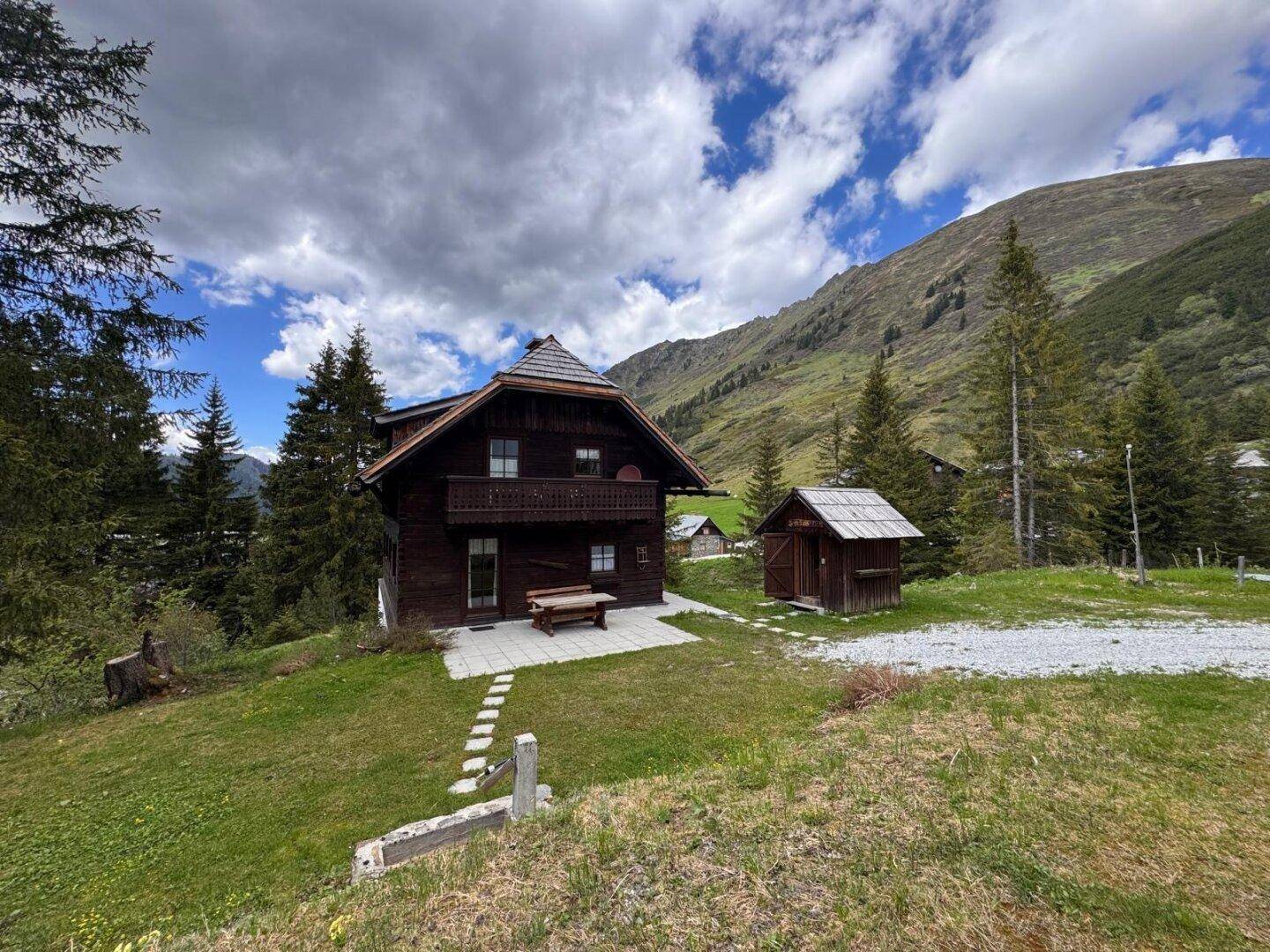 Rustikales Holzhaus mit traditioneller Architektur und Bergblick, umgeben von grüner Natur.