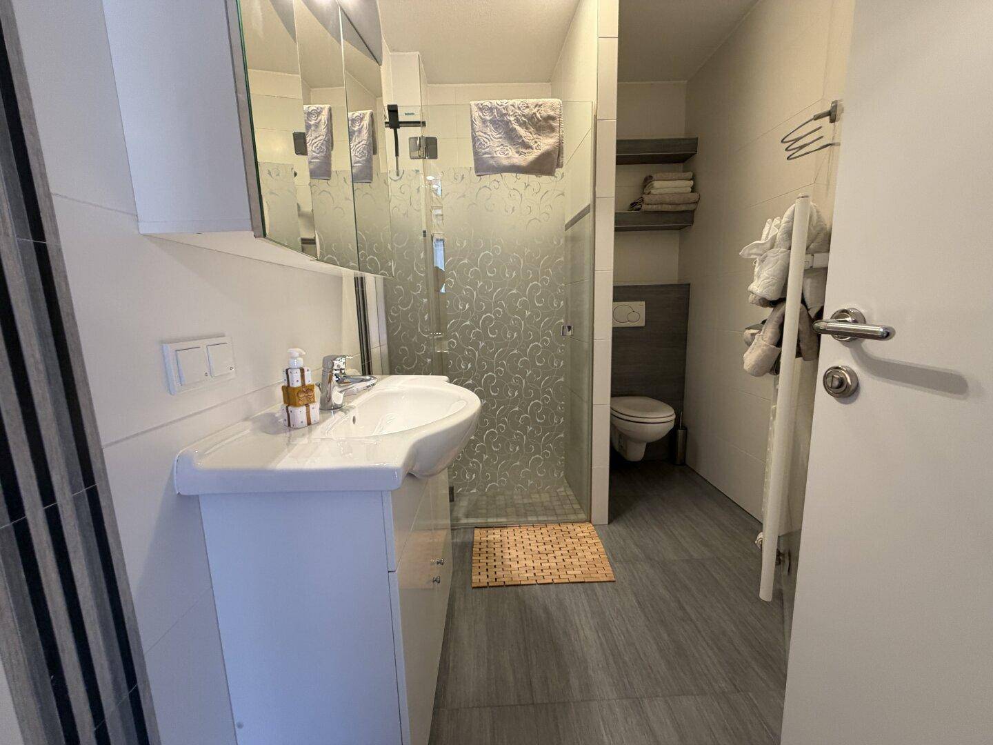 Modernes Badezimmer mit Dusche, Waschbecken und Spiegel, in neutralen Farben gestaltet.