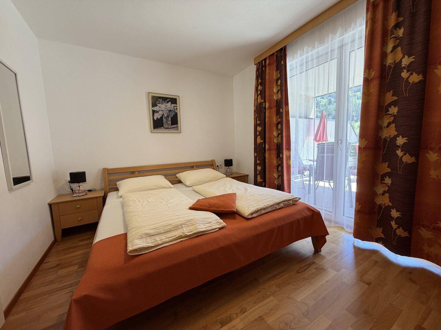 Helles Schlafzimmer mit Doppelbett, Holzboden und direktem Zugang zum Balkon.
