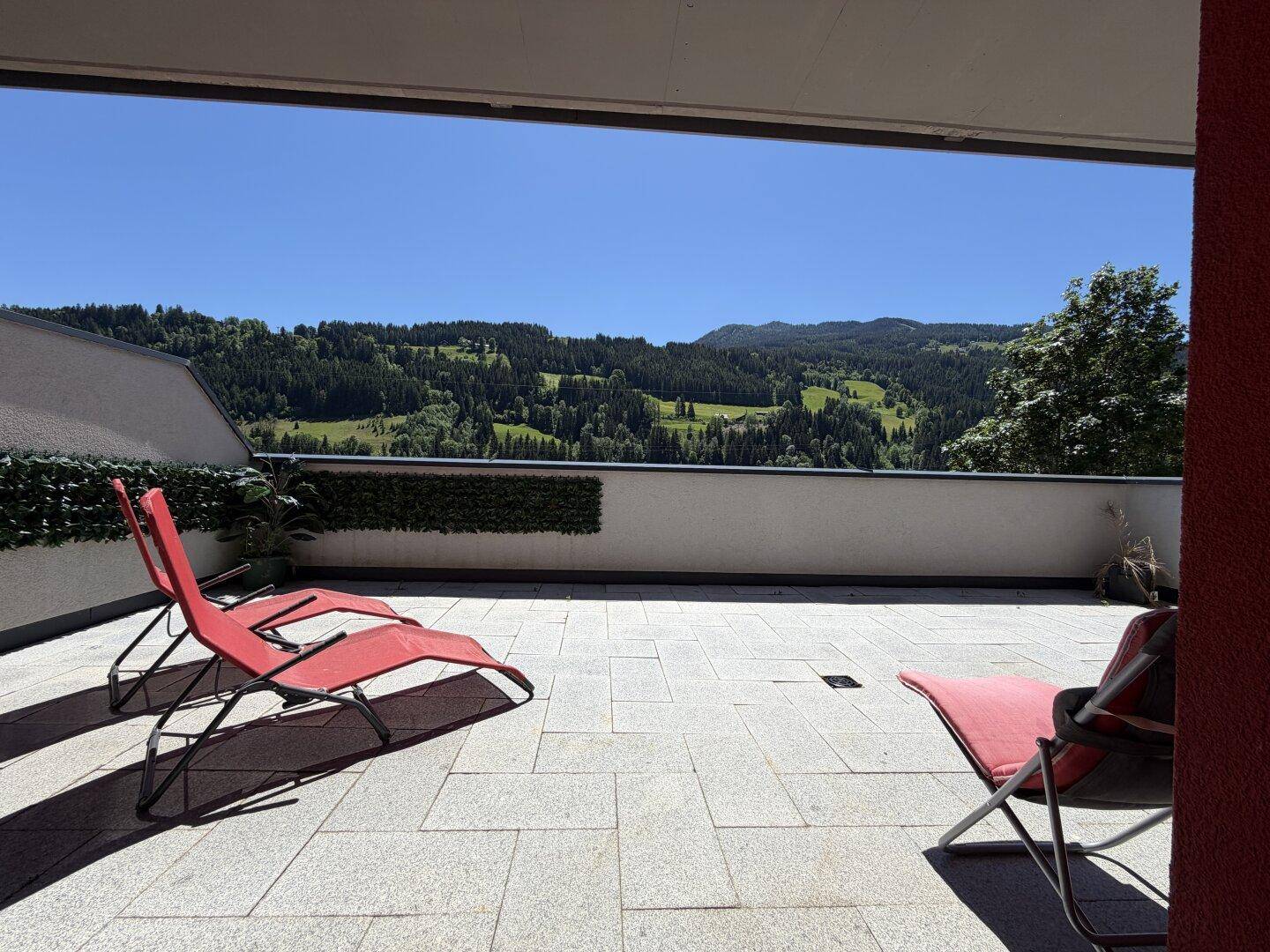 Geräumige Sonnenterrasse mit Liegestühlen und weitem Blick auf die umliegende Berglandschaft.